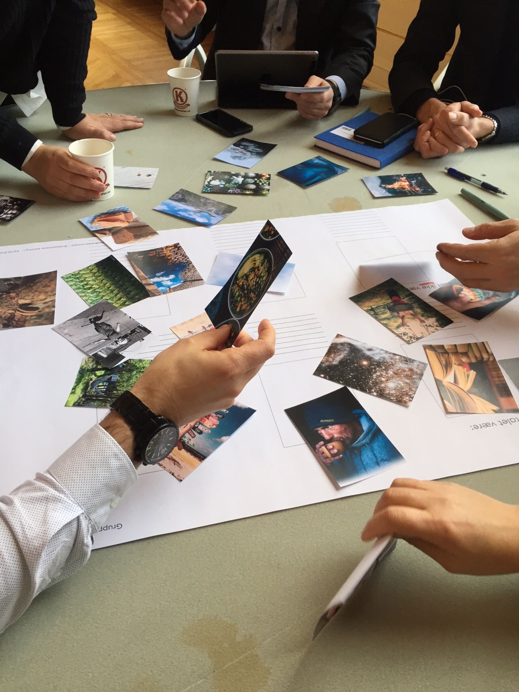 Workshop fra prosjektoppstart. Hender med penner som skriver. Bilder og illustrasjoner plassert på et stort ark. Foto